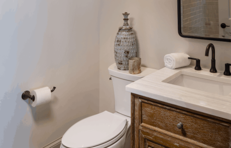 Pool house bathroom features a simple classic look with a rustic-style vanity, white rectangular undermount sink and modern matte black hardware. A dark bronze vintage rounded rectangle pivot mirror and matte black vanity light complement the warm wood console and crisp white walls.