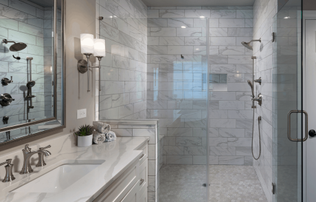 Luxurious master bath remodel features a large walk-in shower with seating bench and niche, frameless glass shower enclosure with hinged door, polished ceramic wall tile in marble white and gray hexagon porcelain mosaic shower floor tile. White shaker vanity with quartz countertops, undermount sink, brushed nickel hardware and sconce lighting.