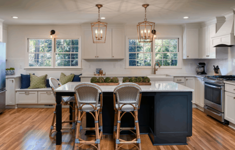 This large modern country kitchen stylishly pairs two toned kitchens cabinets in blue and white. The kitchen island is the focal point with dark blue recessed-panel cabinets, white quartz countertops and a pair of contemporary gold pendant lights above. Complementary white recessed panel cabinets, satin brass hardware, modern white subway tile backsplash and stainless-steel appliances add instant glam to this stunning two-toned kitchen.