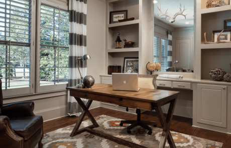 The private home office, painted in Benjamin Moore’s Revere Pewter, features custom built-in book shelves, crown molding and large windows for plenty of natural light. The large classic, freestanding desk, brown leather arm chair and geometric gold and orange rug creates a warm and timeless look.