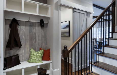 Stylish entry hall with custom built-in storage and white bench, reclaimed wood wall and dark brown wood floors. Gray sliding barn doors lead to laundry room.