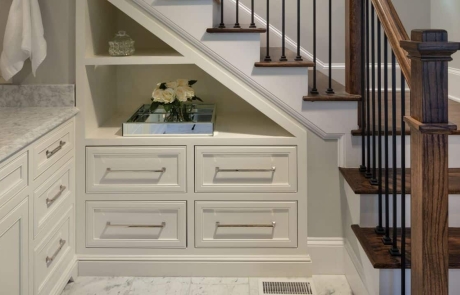 Under stair built-in custom cabinets with open shelving and chrome fixtures. New staircase with brown hardwood steps and black metal balusters.