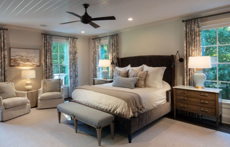 Neutral colored large master bedroom is painted in Benjamin Moore’s Edgecomb Gray with custom trim work, white painted tongue-and-groove ceiling, secret hidden door, dark bronze wall sconces and ceiling fan, brown hardwood floors and designer finishes.