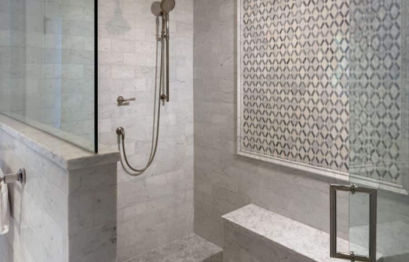 Large frameless glass shower & seating bench with polished nickel fixtures, Carrera Bianco marble tile walls and ceiling and gray marble lattice mosaic accent wall.