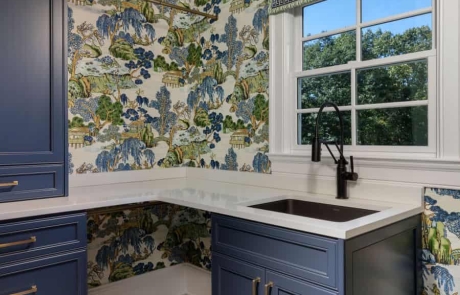 Blue, green & white laundry room addition with blue custom shaker cabinets and bronze hardware, white hexagon porcelain mosaic floor, drying station, black undermount laundry sink with matte black pull-out spray faucet.