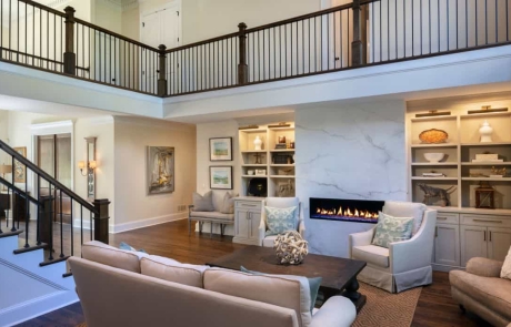 Keeping room renovation includes a floor to ceiling porcelain slab linear fire feature and custom white built-in cabinetry and trim work, brown hardwood floors and new staircase with brown hardwood steps and black metal balusters.