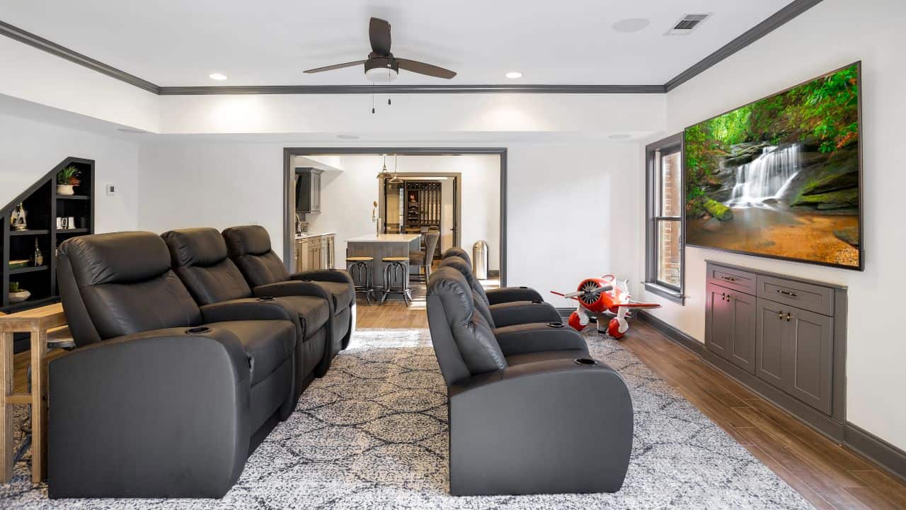 A basement home theater was a must in this custom basement remodel complete with comfortable gray leather stadium seating, large mounted flat screen TV and a high performing audio system.