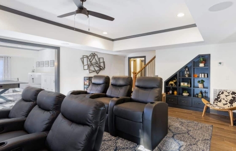 Large modern concept basement renovation with home theater and adjoining game room with black custom under stair built-ins & drawers and a tripod mid-century modern chair upholstered in authentic hide fur.