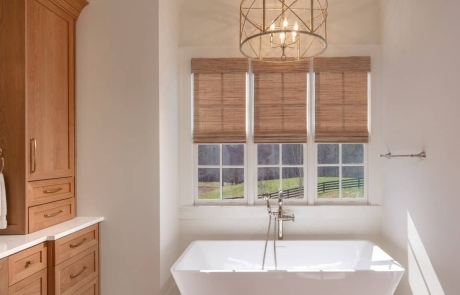 Master bathroom features a white rectangular freestanding soaker tub centered in front of large windows, with white quartz countertops and light wood shaker cabinetry.
