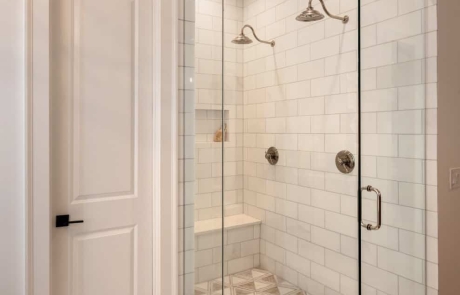 The frameless glass shower enclosure with hinged door boasts dual rain shower heads with separate controls, built-in bench and shampoo niche and a marble tile mosaic shower floor.