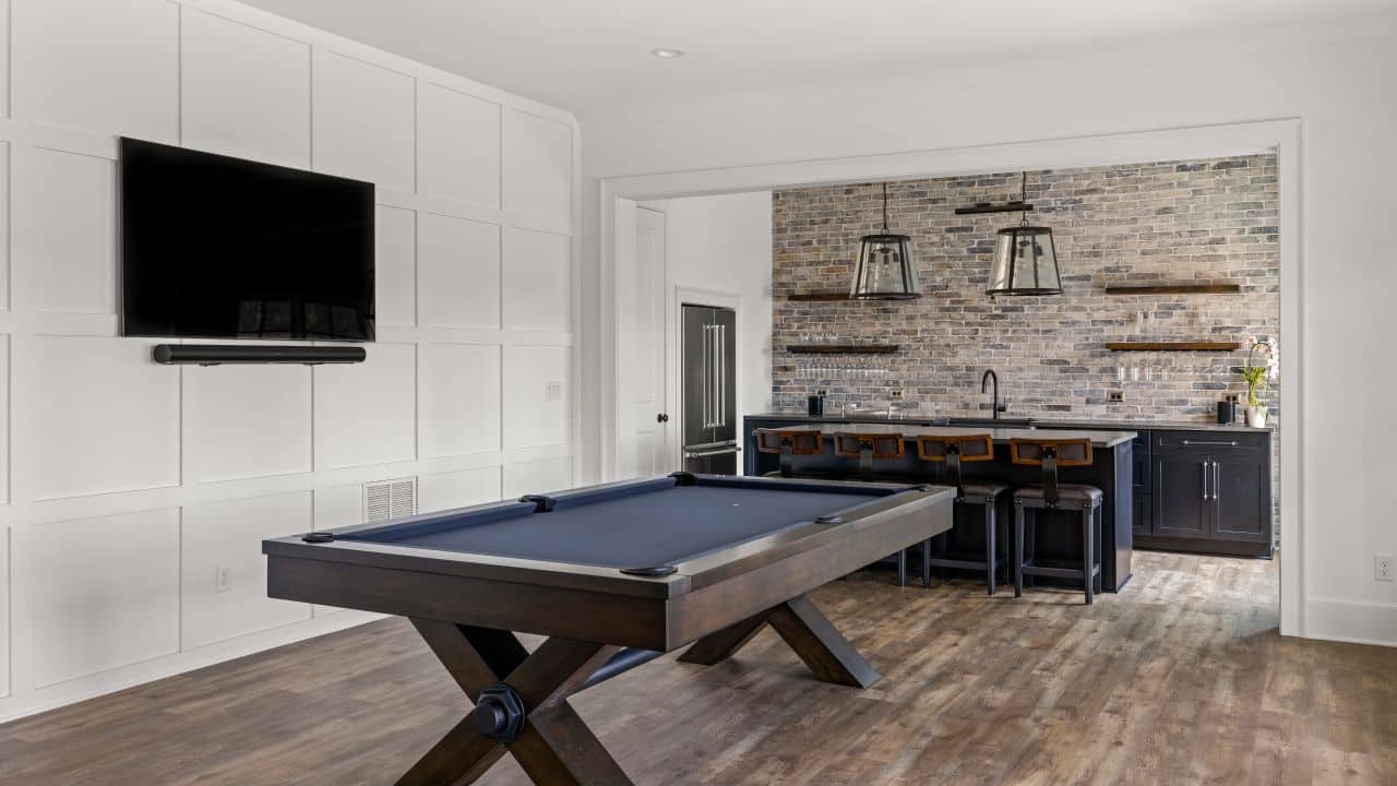 Sophisticated black bar and billiard room with decorative trim paneling walls and mounted tv, black shaker cabinets, grey reclaimed brick backsplash, black pearl leathered granite countertops.