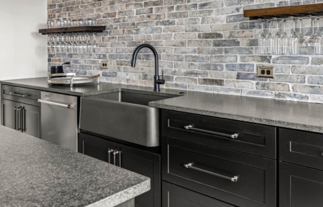 Custom designed bar with black shaker cabinets, grey reclaimed brick backsplash, black pearl leathered granite countertops, stainless steel apron sink, reclaimed wood wine shelves.