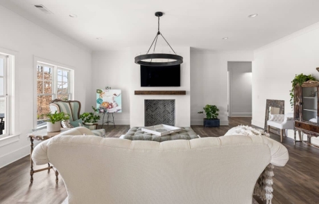 Custom basement remodel features a family room with white plaster fireplace and reclaimed wood mantle, white couch, brown floors and vintage decor.