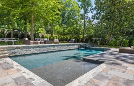 Backyard Swimming Pool Design with Flush Spa & Spillover, Large Tanning Ledge, Midnight Blue PebbleTech Pool Finish, Stacked Stone Raised Beam, Upper & Lower Paver Patios, & Luxury Pool Features.