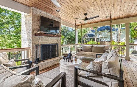 Luxurious cedar covered porch features a relaxing seating area centered around a Lueders limestone fireplace with mounted tv, cedar Tongue & Groove ceilings, modern furnishings and a gorgeous hanging porch swing bed.