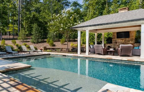 Luxury swimming pool installation and custom-built pool house surrounded by a spacious paver patio and pool landscaping.