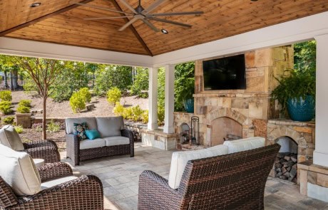 Poolside cabana includes a large outdoor living room with comfortable seating, a stacked stone fireplace and hearth with outdoor tv, Belgard paver patio, vaulted tongue & groove ceiling, can lighting, & large outdoor ceiling fans.