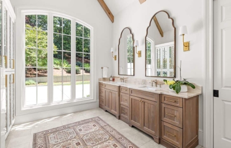 Modern farmhouse bathroom with vaulted ceiling, custom double vanity in natural wood, gold arched mirrors, quartz countertops, luxury bathroom tile and sconce lighting fixtures.