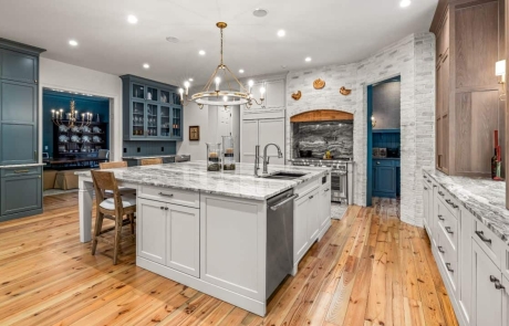 High-end kitchen design includes custom cabinetry with Shaker style cabinet doors, Steel Gray granite island and countertops, built-in beverage station with dual glass wine fridges, professional-grade appliances and wide plank wood flooring.