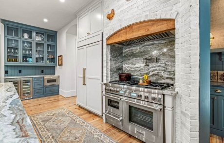 Luxury kitchen remodel features two-toned cabinets with custom glass-fronts and built-in storage solutions, lime-washed brick accent wall, wood beam range hood, statement kitchen backsplash, 48-Inch Dual-Fuel Pro Grand® Range, and panel ready appliances.