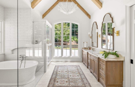 Luxury master bathroom renovation includes vaulted ceiling with a white and natural wood bathroom aesthetic, spa-like wet room with floor to ceiling white subway tile walls, freestanding soaking tub and high-end bathroom features.