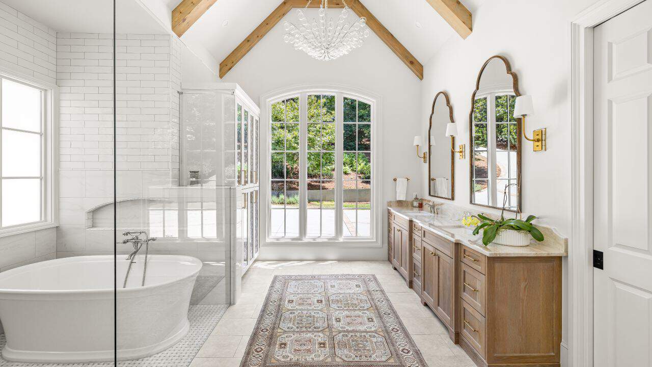 Luxury master bathroom renovation includes vaulted ceiling with a white and natural wood bathroom aesthetic, spa-like wet room with floor to ceiling white subway tile walls, freestanding soaking tub and high-end bathroom features.