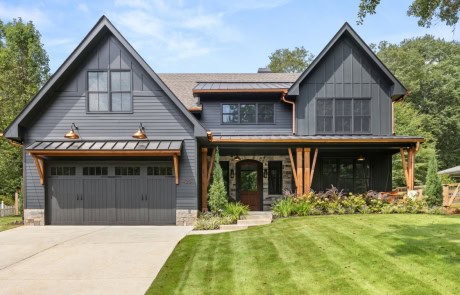 Custom modern farmhouse with dark board and batten siding, copper accents, wood beams, and landscaped curb appeal.