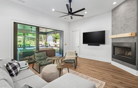 Modern living room in custom home build, featuring a minimalist concrete fireplace with a natural wood mantel, and sliding glass doors opening to an outdoor living area.