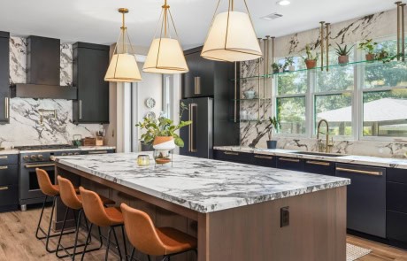 Modern kitchen with marble countertops, black cabinetry, brass hardware, and a large island for seating.