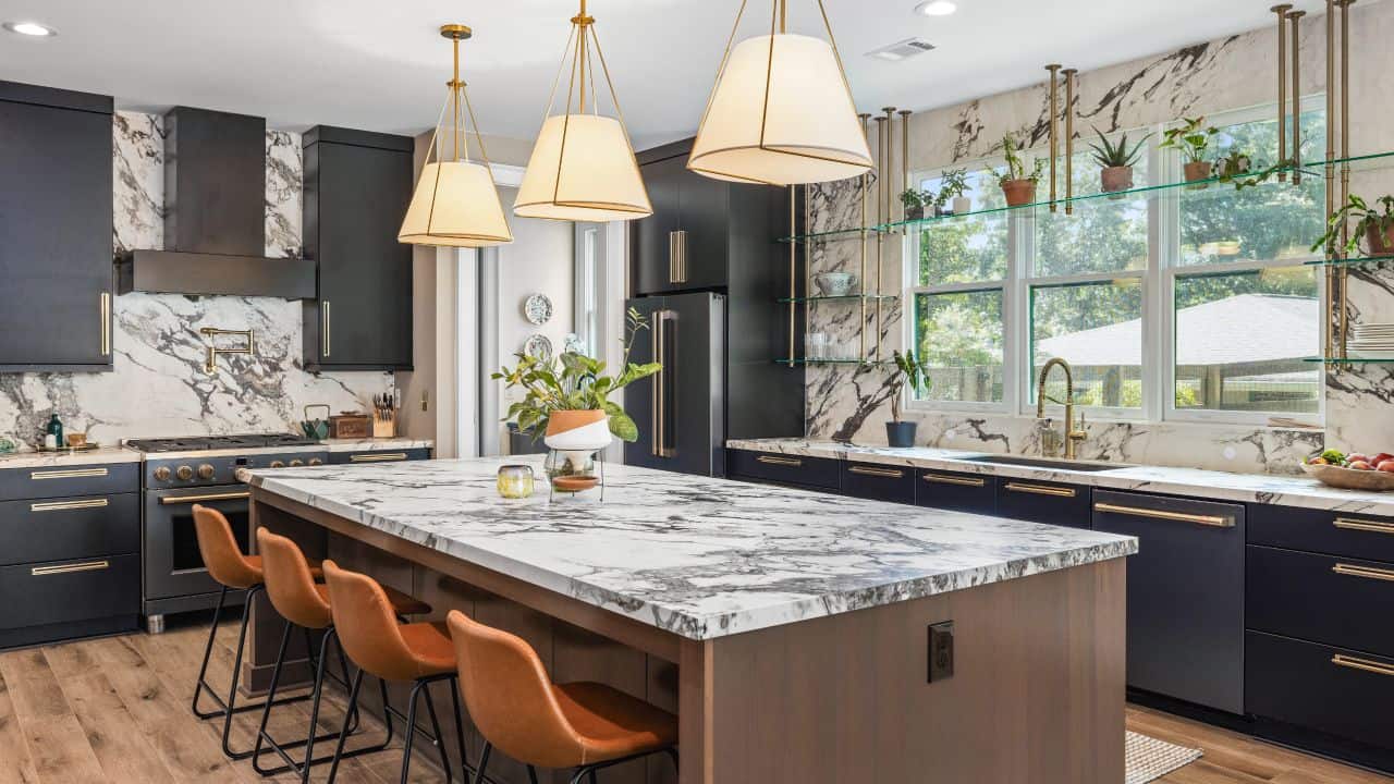 Modern kitchen with marble countertops, black cabinetry, brass hardware, and a large island for seating.