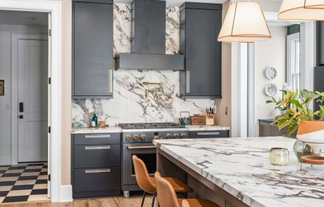 Elegant kitchen with black cabinetry, a floor-to-ceiling marble backsplash, a luxury gas range with brass hardware, and a marble island with dramatic veining and waterfall edges.