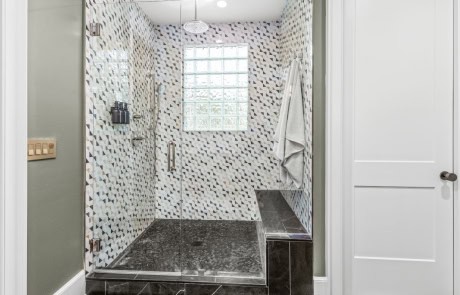 Master bathroom includes a spacious shower with geometric tile walls, a glass door, built-in bench, glass block window for natural light, and a luxurious black marble tile floor.