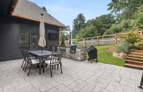 Outdoor living space designed for entertaining includes a paver patio with dining area, mounted TV, built-in grill station, and a Green Egg for versatile cooking.